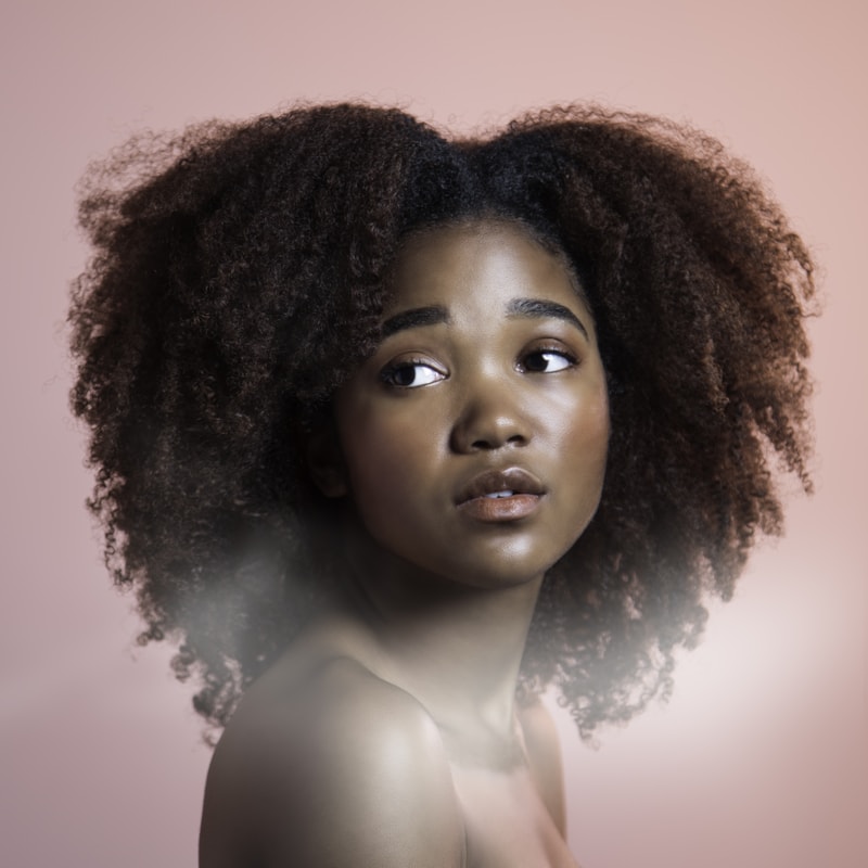 Close portrait of a model against a warm neutral ground, natural hair backlit
