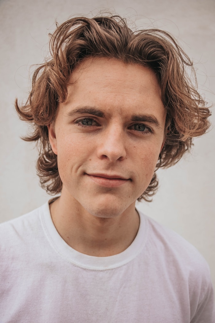 Male model photographed against a pale stone wall in soft daylight