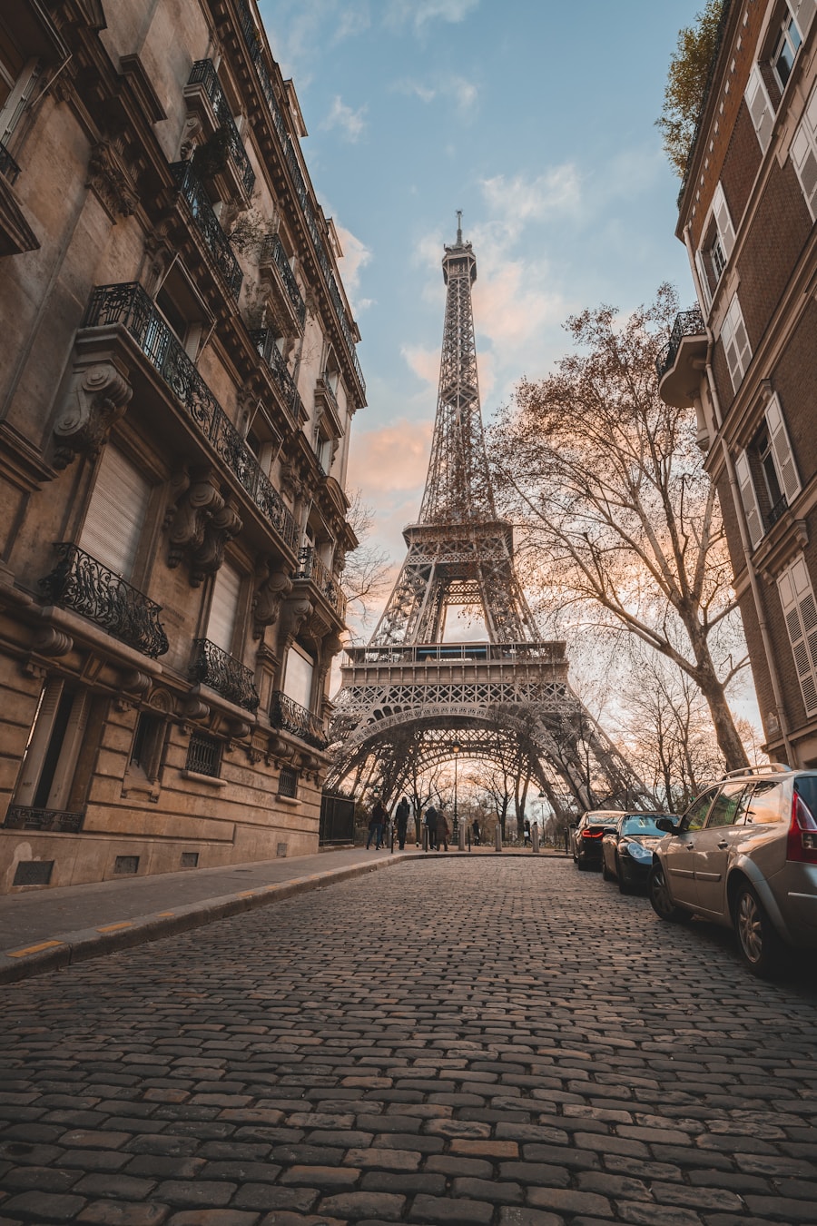 A quiet Paris street at dusk with an iron tower rising beyond the rooftops
